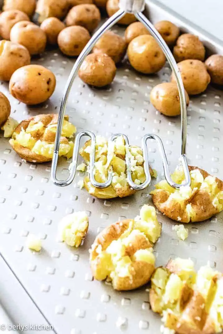 Potato masher mashing potatoes on a pan.