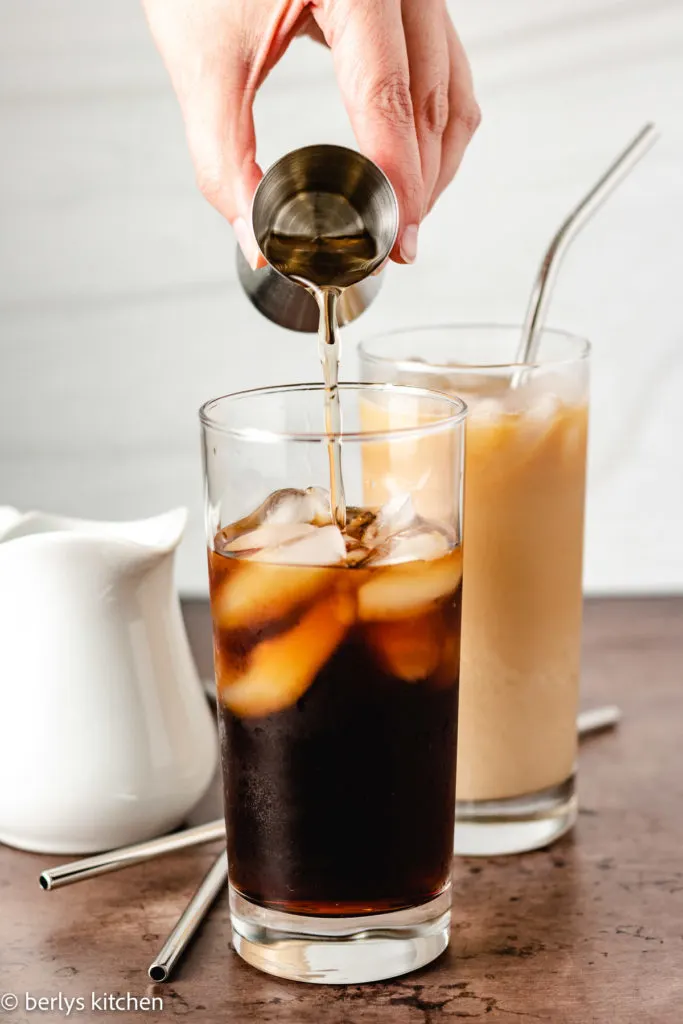 Caramel syrup being poured into a glass of coffee.