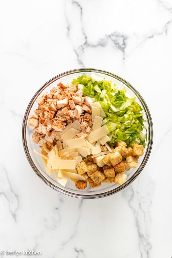 Top down view of chicken, lettuce, cheese, and pasta in a bowl.