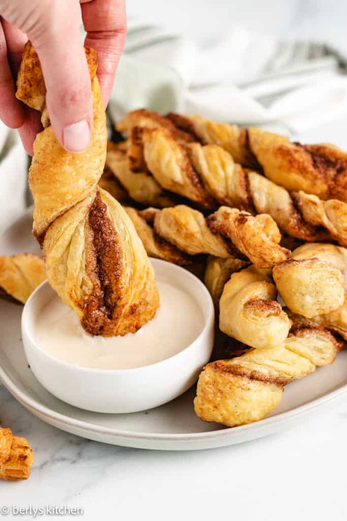 Cinnamon twists being dunked into icing.