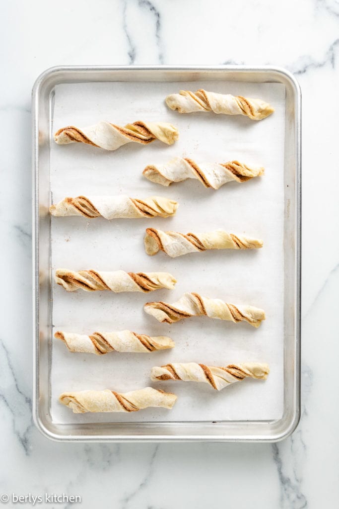 Top down view of unbaked cinnamon sticks on a baking sheet.