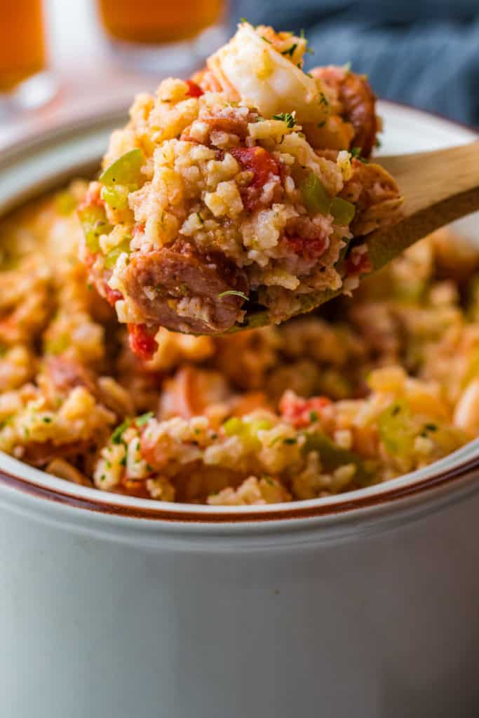 Wooden spoon scooping jambalaya from a gray container.
