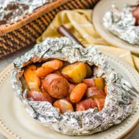 Serving of sausage and potatoes foil packet on a tan plate.