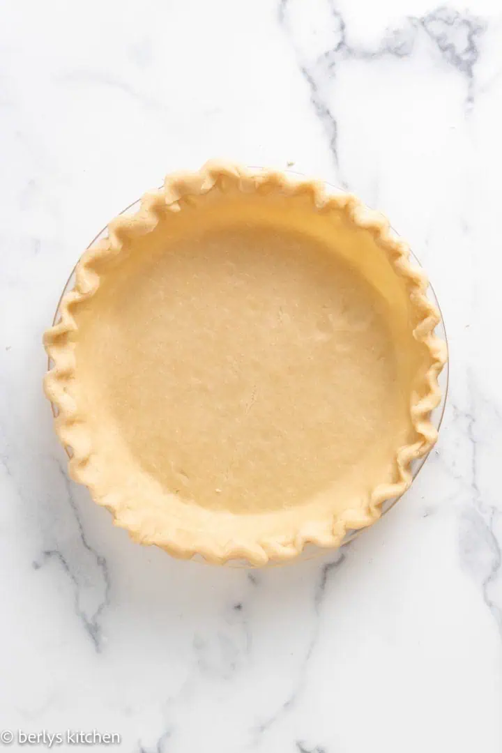 Top down view of unbaked pie crust with butter in a pan.