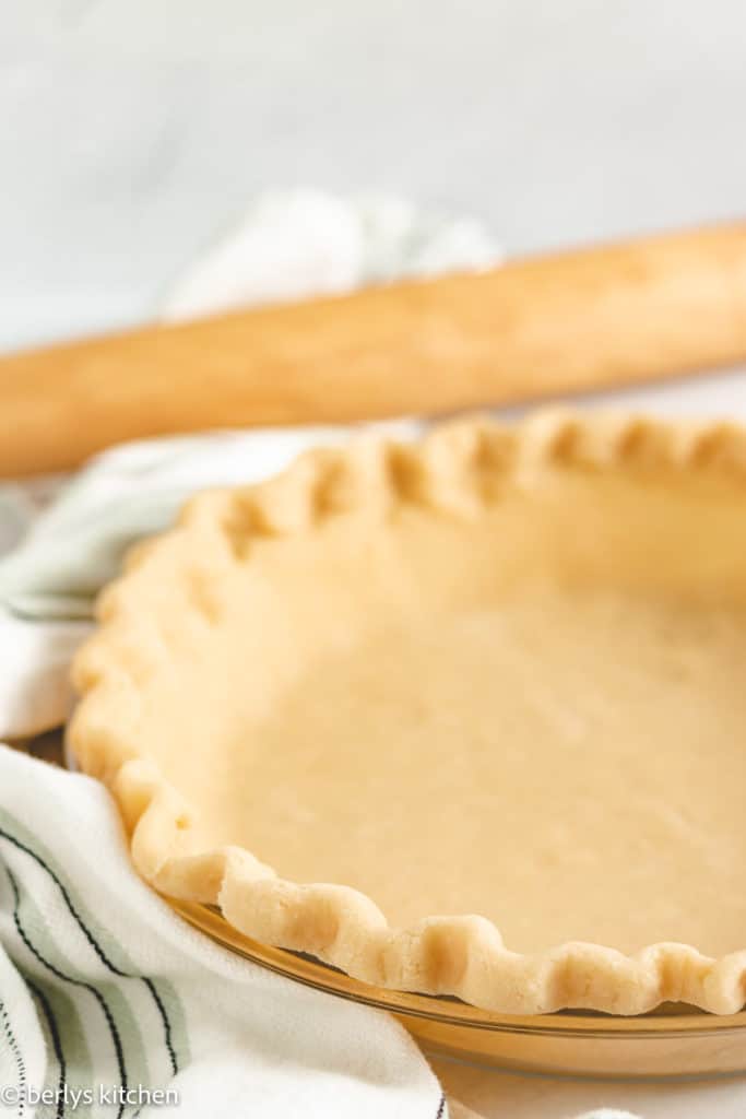 Pie crust with butter next to a rolling pin.