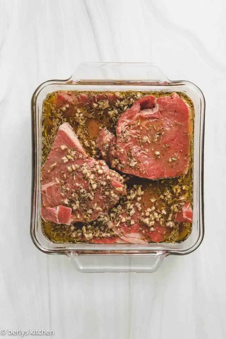 Several pieces of steak marinating in a pan.