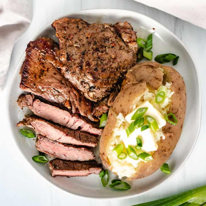 Top down view sirloin steak and bake potato with green onions.