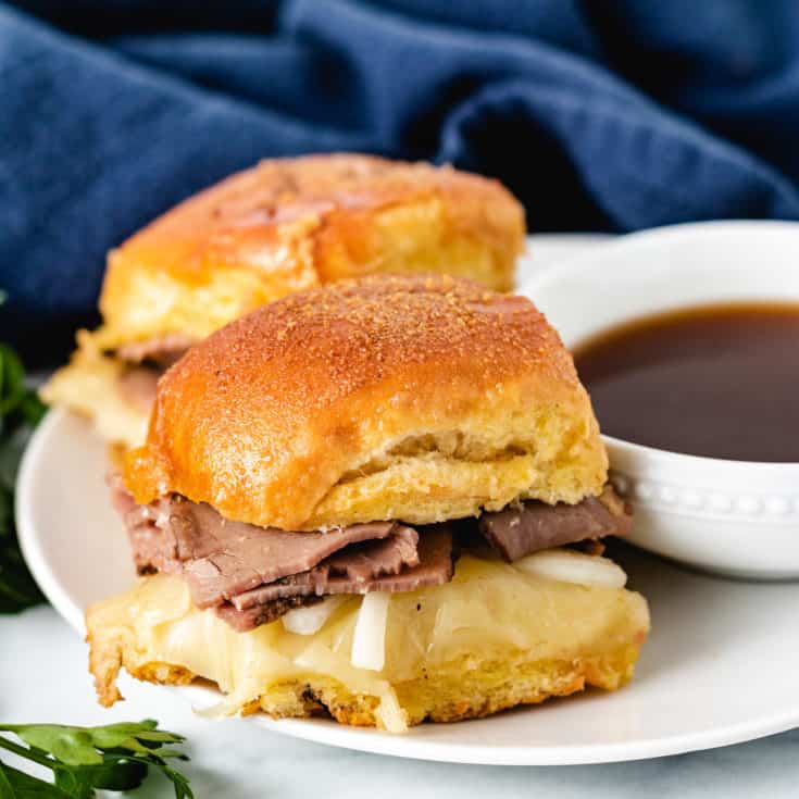 Two sliders on a plate with au jus.
