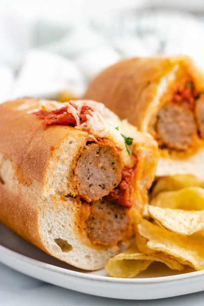 Two half meatball sub sandwiches with potato chips.