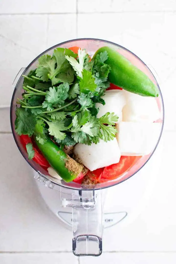 Top down view of ingredients for salsa in a food processor.