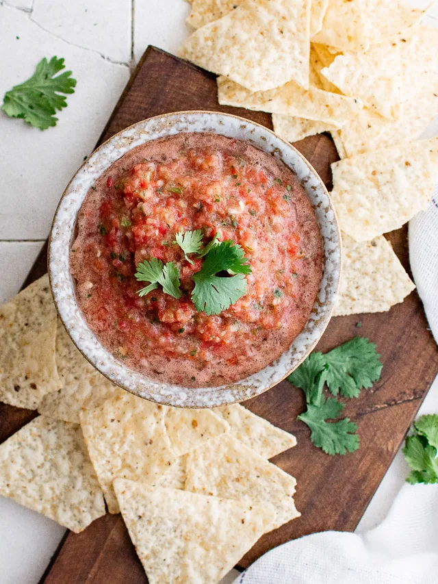 Top down view of salsa and chips on a wooden board.