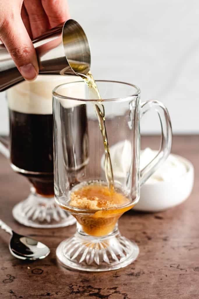 Whiskey being poured into a glass mug.