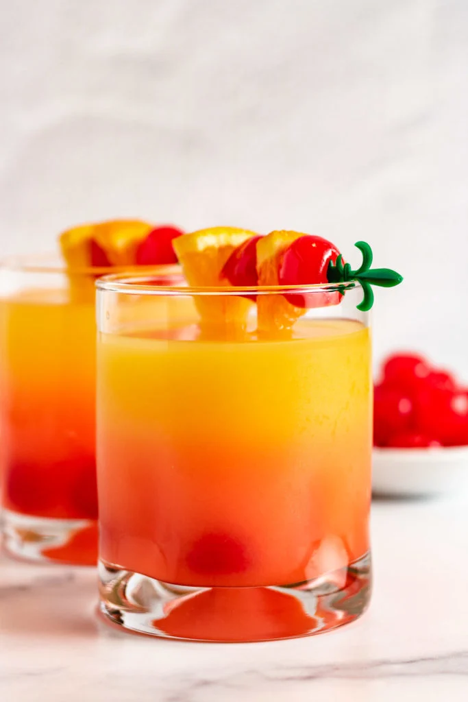 Two rum mixed drinks with orange and cherry garnish.