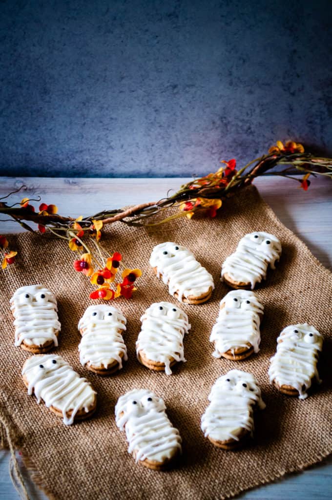 Several nutter butter mummy cookies on brown burlap.