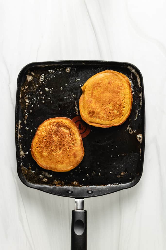Top down view of pumpkin pancakes cooking on a pan.