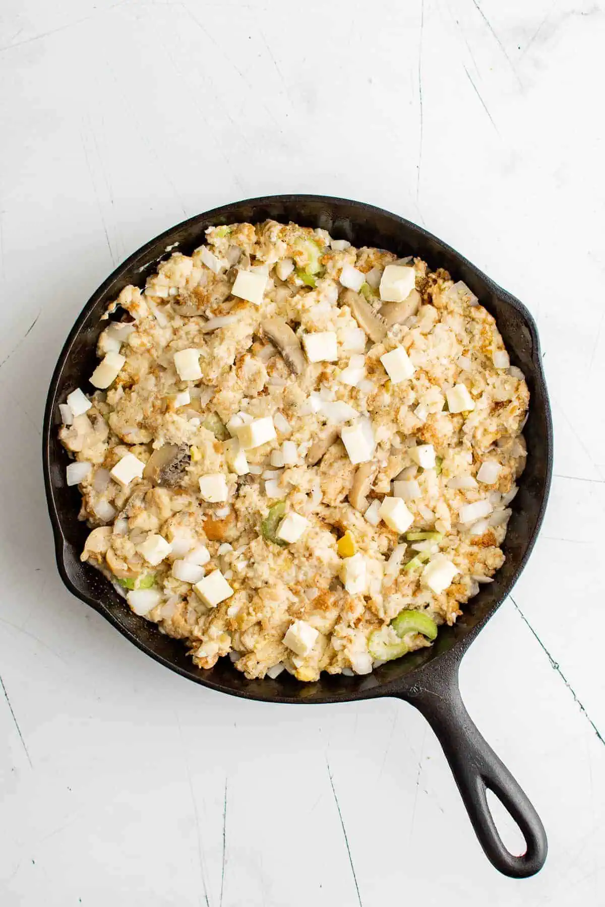 Unbaked stuffing in cast iron dotted with butter.