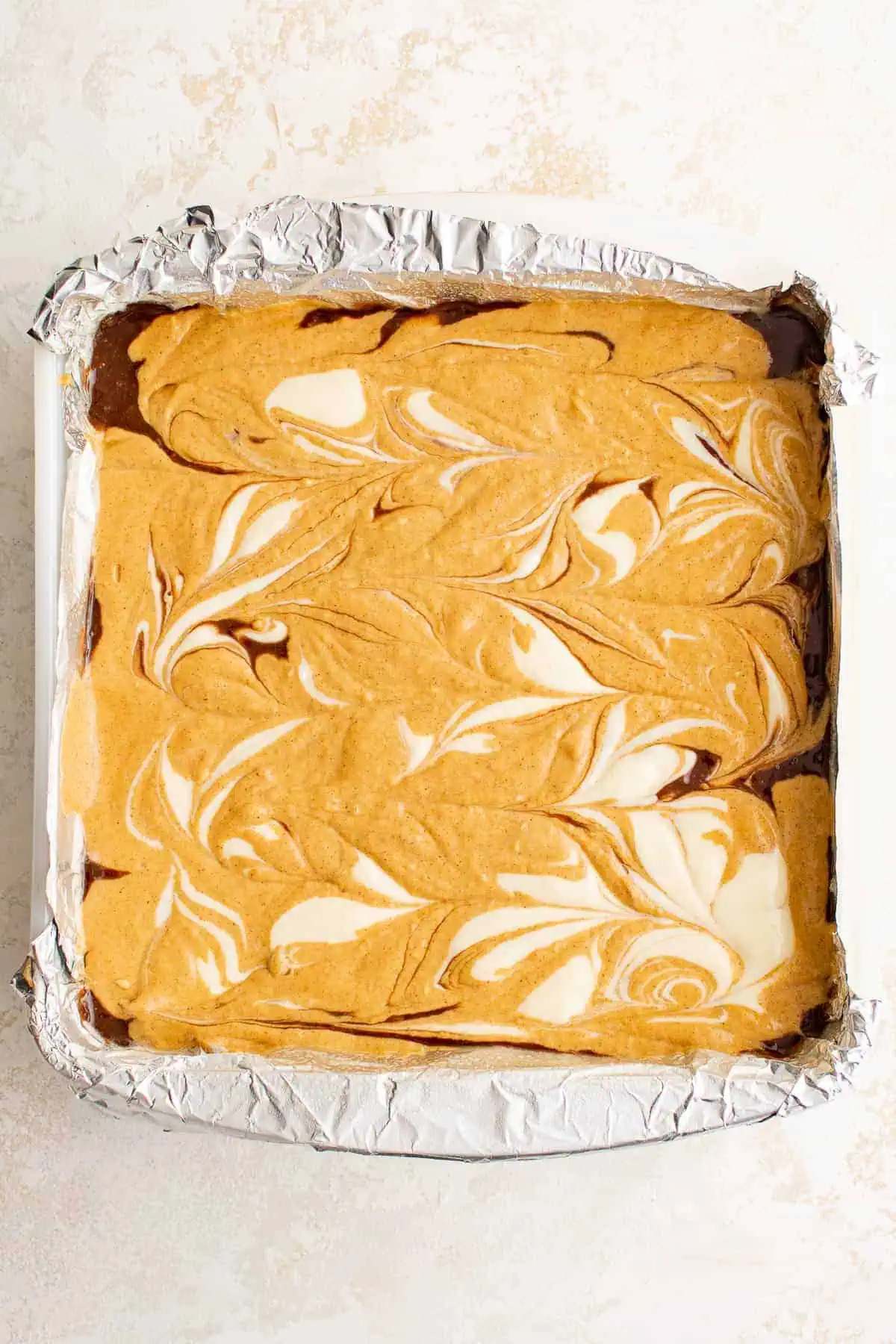 Top down view of swirled cream cheese on top of unbaked brownies.