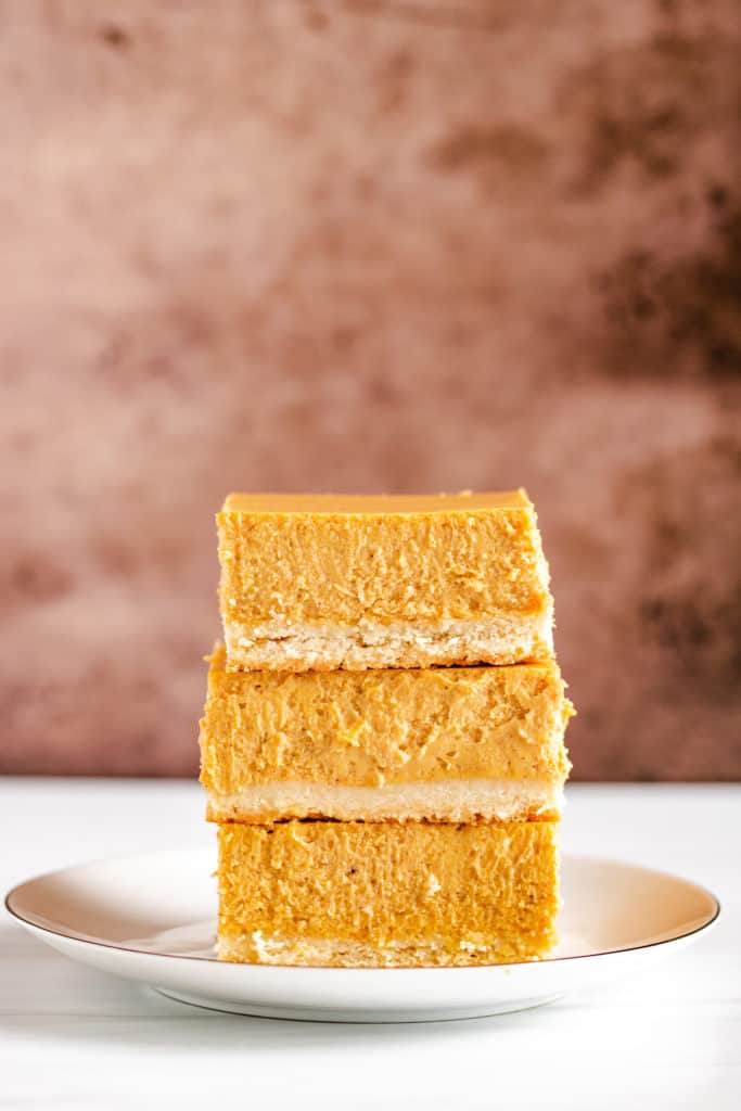 Stack of 3 pumpkin cheesecake bars on a plate.