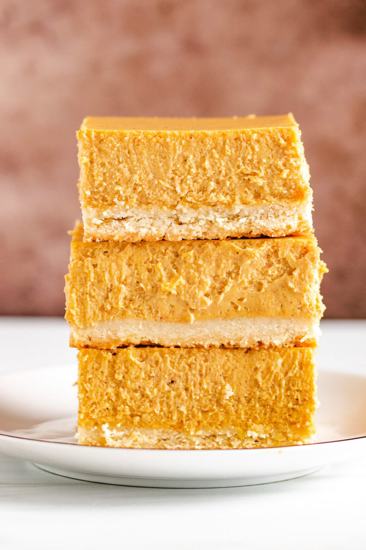 Stack of 3 pumpkin cheesecake bars on a plate.