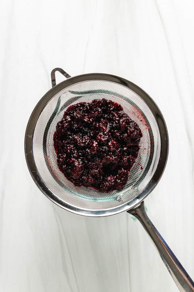 Blackberry pulp being poured through a mesh sieve.