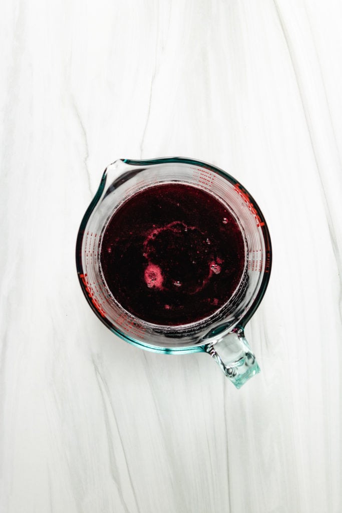 Top down view of strained blackberry syrup in a measuring cup.