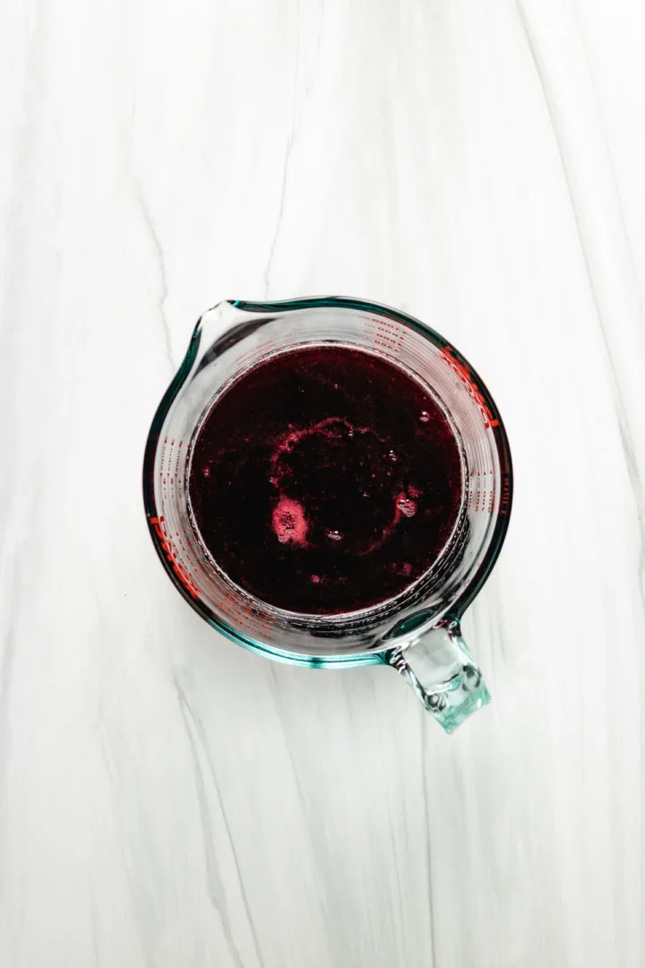 Top down view of strained blackberry syrup in a measuring cup.