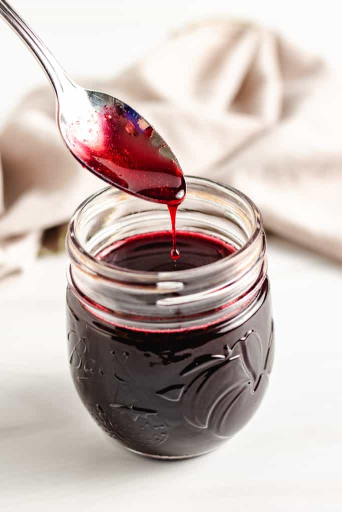 Spoon being dipped into blackberry simple syrup.