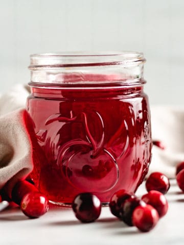 Cranberry simple syrup in a jar with fresh cranberries.