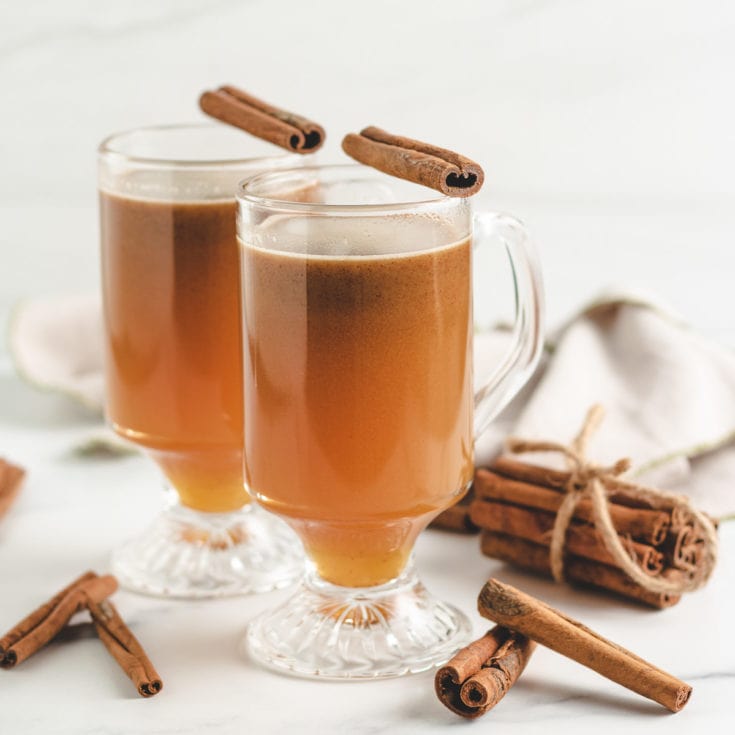 Two glasses of hot buttered rum with cinnamon sticks on top.