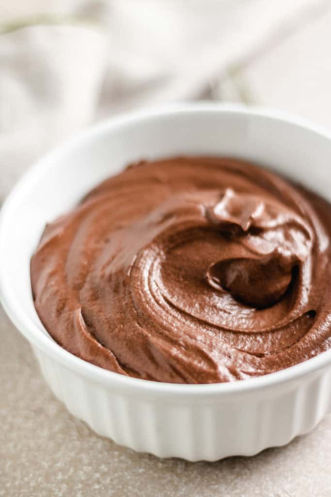 Close up view of chocolate frosting in a white dish.