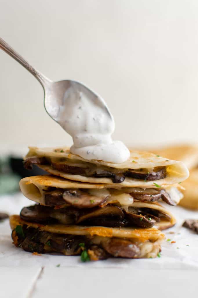 Spoon putting sour cream on a quesadilla.