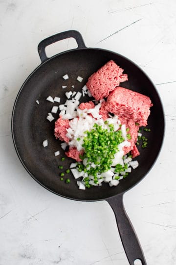 Raw ground beef, jalapenos, and onions in a pan.