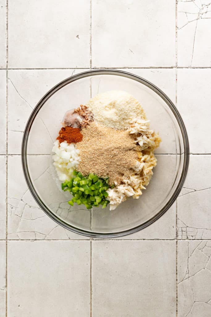 Breadcrumbs, seasoning, crab, egg, cheese, and bell pepper in a bowl.