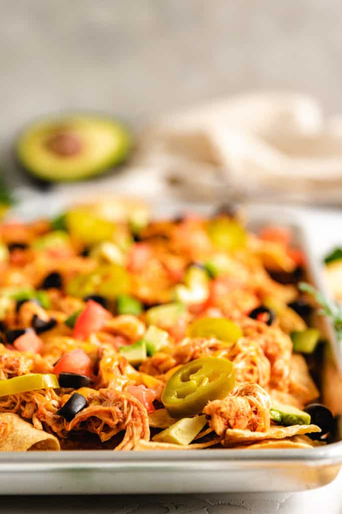 Baking sheet piled with crockpot chicken nachos.