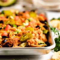 Side view of crockpot chicken nachos on a metal pan.