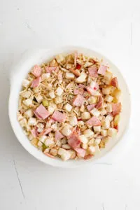 Potatoes, cheese, Canadian bacon, salt, pepper and chili powder stirred in a baking dish.
