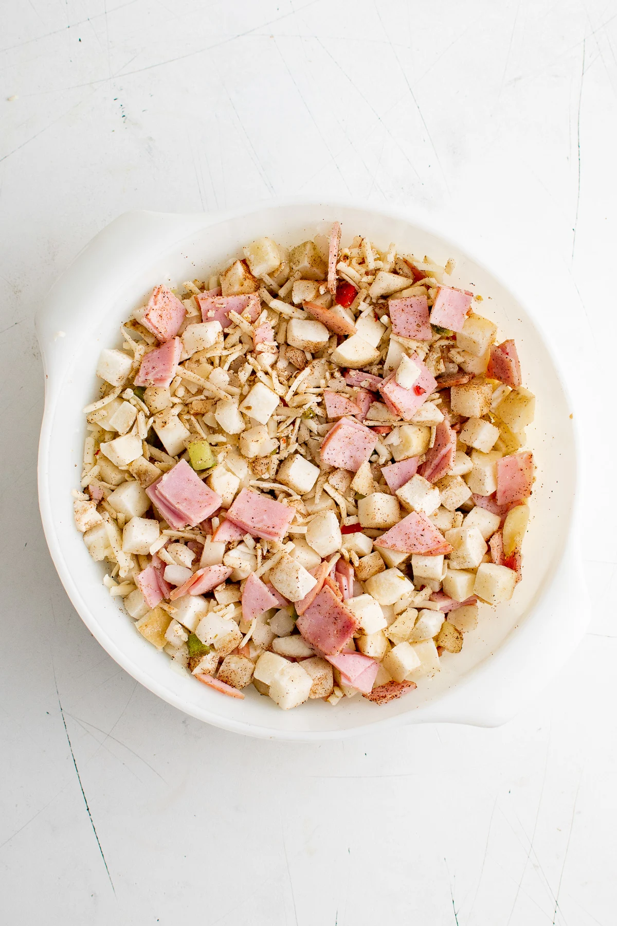 Potatoes, cheese, Canadian bacon, salt, pepper and chili powder being stirred in a baking dish.