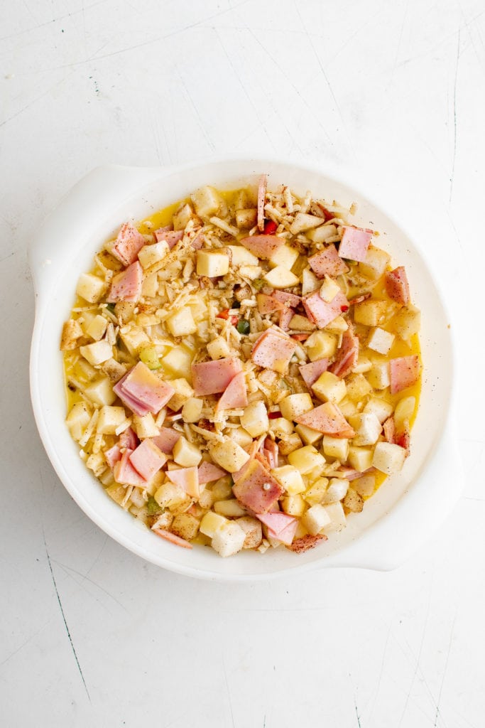 Eggs added to potatoes, cheese, Canadian bacon, salt, pepper and chili powder in a dish.