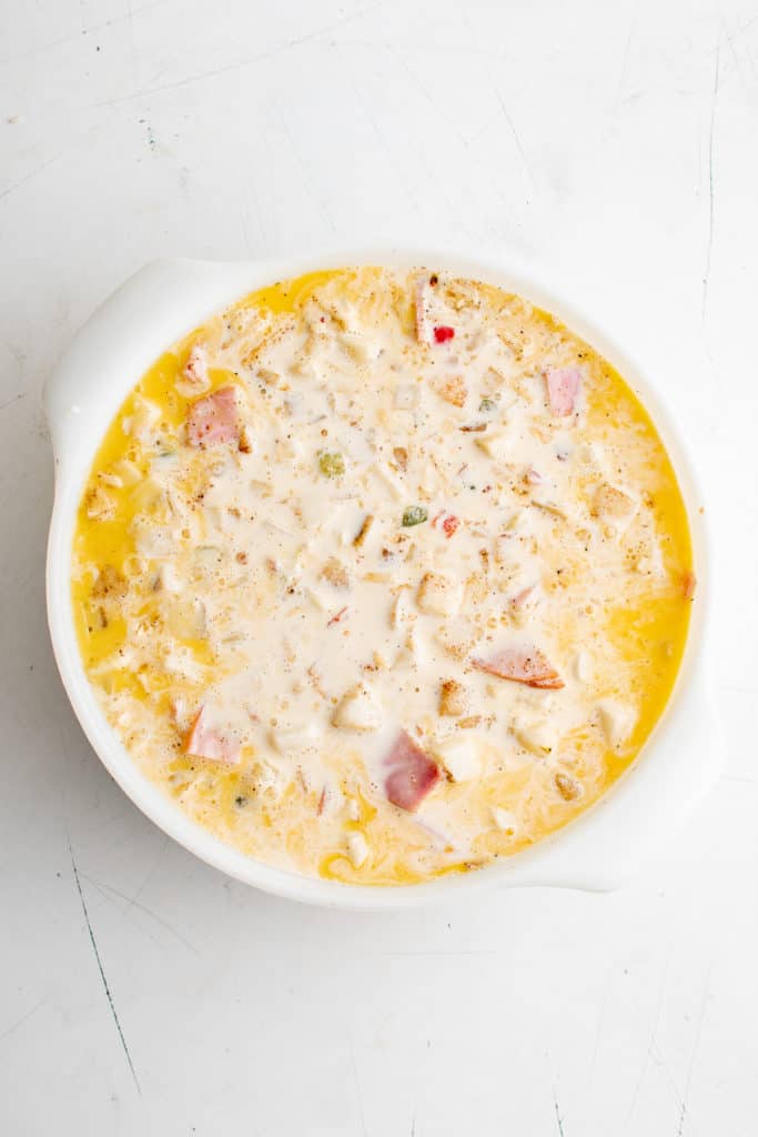 Milk added to eggs, potatoes, cheese, Canadian bacon, salt, pepper and chili powder in a baking dish.