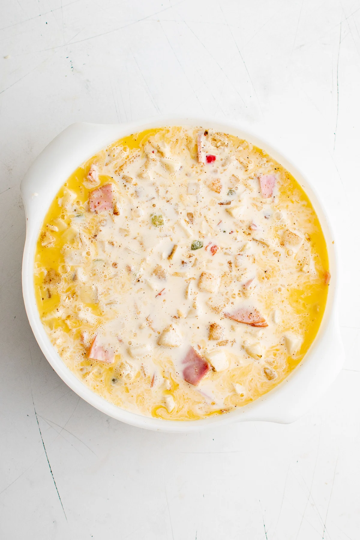 Milk being poured into eggs,&nbsp;potatoes, cheese, Canadian bacon, salt, pepper and chili powder in a baking dish.