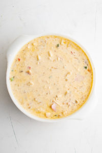 Milk, eggs, potatoes, cheese, Canadian bacon, salt, pepper, and chili powder stirred together in a baking dish.