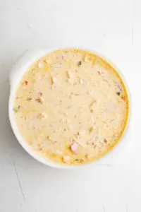 Milk, eggs, potatoes, cheese, Canadian bacon, salt, pepper, and chili powder stirred together in a baking dish.