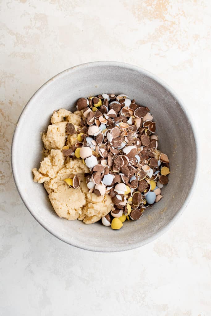 Crushed mini egg candy in a bowl of cookie batter.