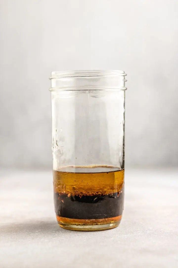 Olive oil added to a jar of balsamic vinegar and seasonings.