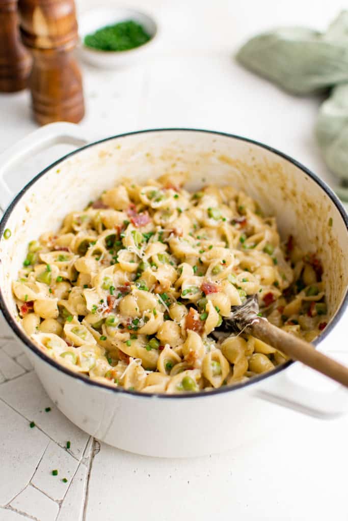 White pan filled with pasta and a wooden spoon.