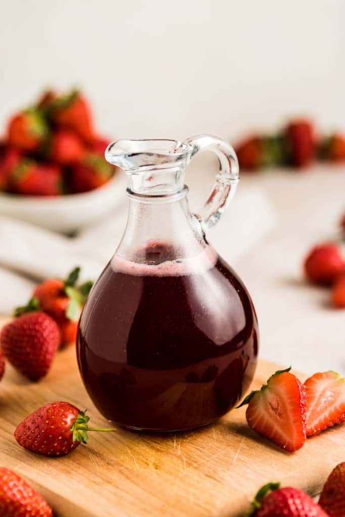 Curet of strawberry simple syrup next to fresh berries.