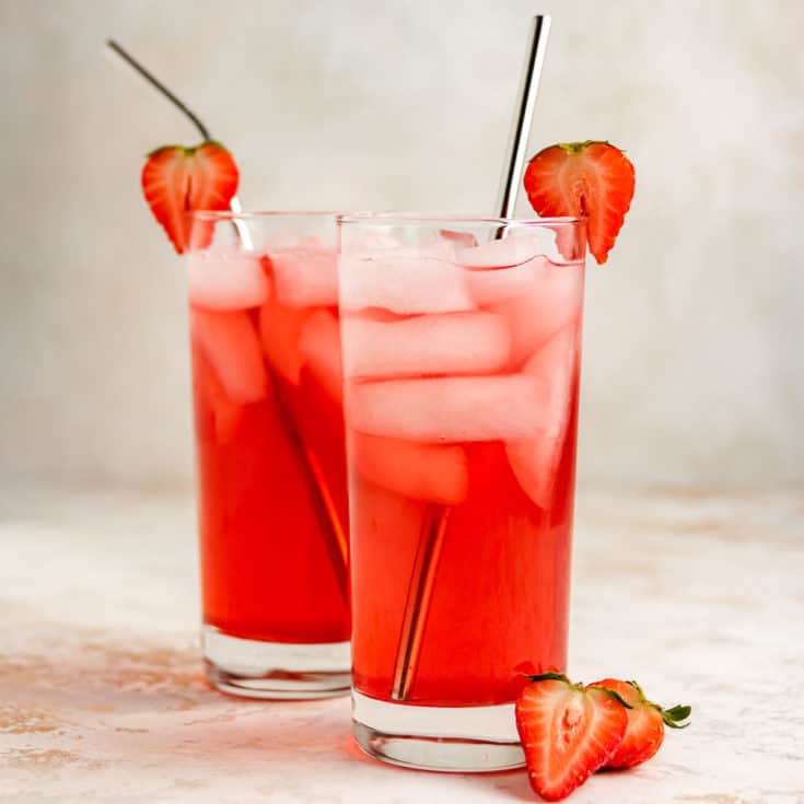 Two glasses of strawberry soda with metal straws.