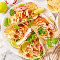 Fish tacos with cilantro, lime, and radish slices on a plate.