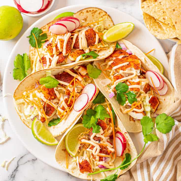 Fish tacos with cilantro, lime, and radish slices on a plate.
