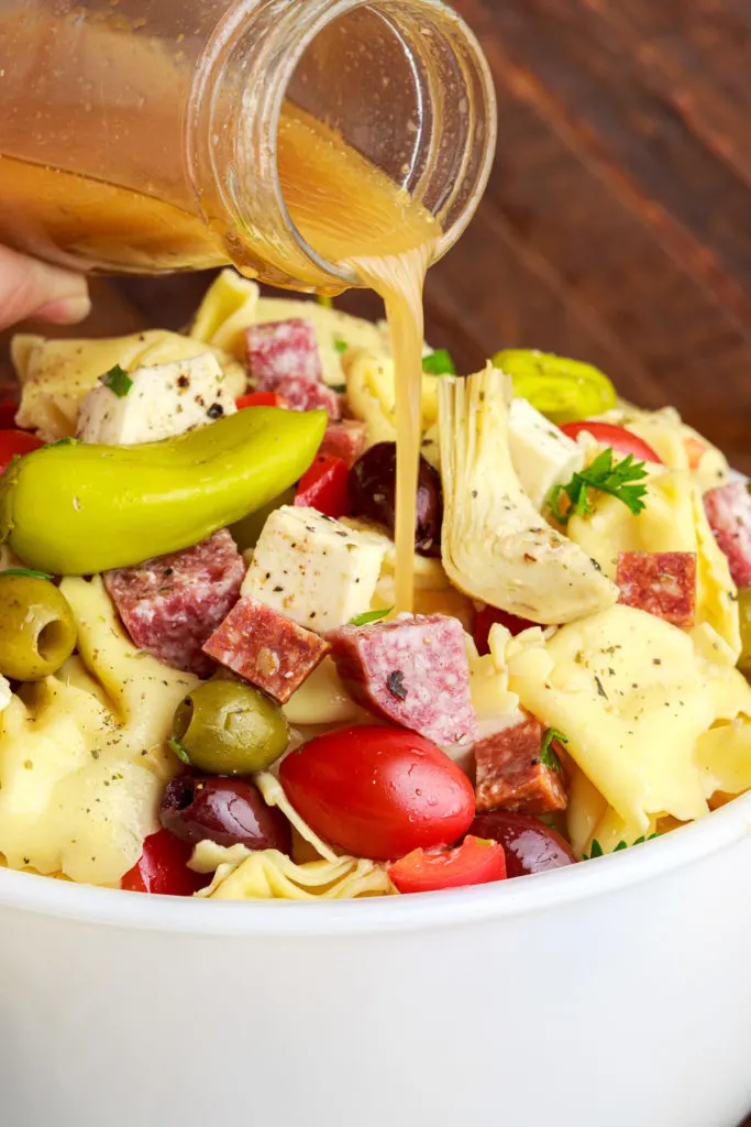 Dressing being poured over tortellini pasta salad.